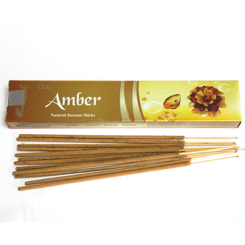 Smilkalai Amber – ilgų rudi kvapiųjų lazdelių rinkinys prieš auksinę dėžutę, pabrėžia natūralų gintaro aromatą ir lazdelių ilgį