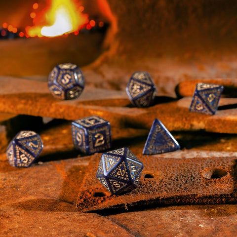 RPG kauliukai: mėlynas metalinis 7 dalių rinkinys su auksiniais skaičiais, 20‑sienis priekyje ant rūdinto krosnies fono