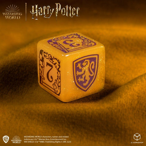 Kauliukas Harry Potter auksinis su violetiniu liūto herbu ir skaičiumi 7, blizgus marmurinis paviršius, kampinis artimas planas
