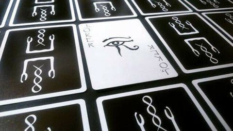 Tarot kortos juodais nugarėlėmis, viena balta korta su Horuso akies simboliu ryškiai atversta