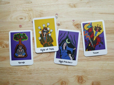 Taro kortos — keturios spalvotos iliustracijos (Hermit, Eight of Think, High Priestess, Tower) išdėstytos ant šviesaus medinio fono
