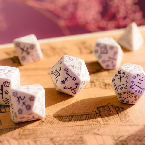 Dvidešimtkampiai kauliukai baltos spalvos su violetiniais japoniškais simboliais ir vyšnių žiedų raštu, artimas kampinis vaizdas ant medinės žaidimo lentos