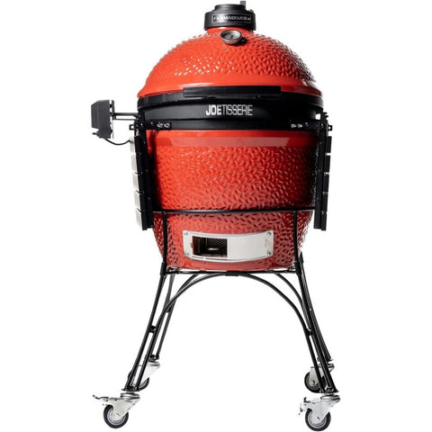 Kamado grilis JoeTisserie raudonas, pilno dydžio ant juodo stovo su ratukais ir sumontuotu rotiserijos varikliu, matomas priekis