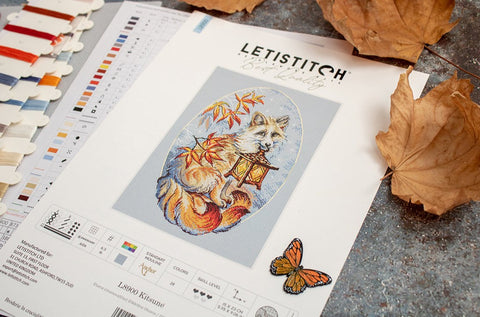 Siuvinėjimo rinkinys Letistitch su lapės motyvu, spalvų lentele ir siūlų kortelėmis ant stalo, rudeniški lapai ir drugelis šone