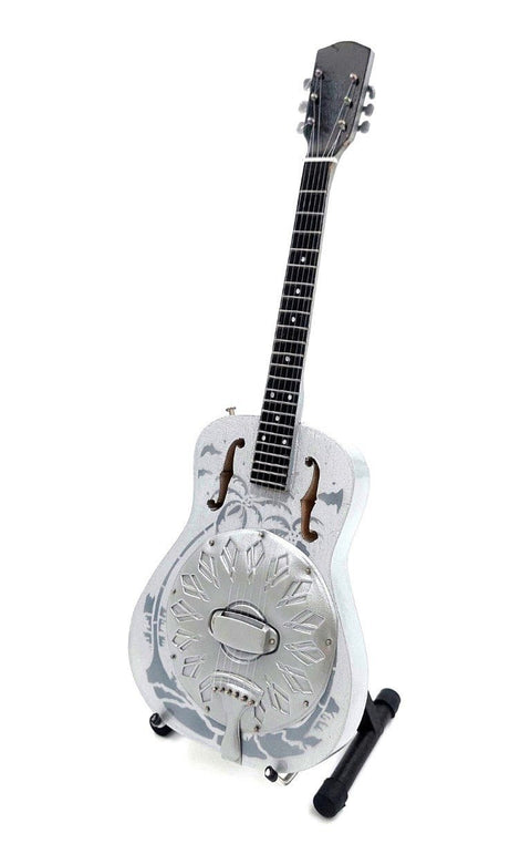 Rezonatorinė gitara sidabro‑balta su apvaliu metaliniu rezonatoriumi ir dekoratyviniu raštu, trijų ketvirčių priekinis kampas ant stovo