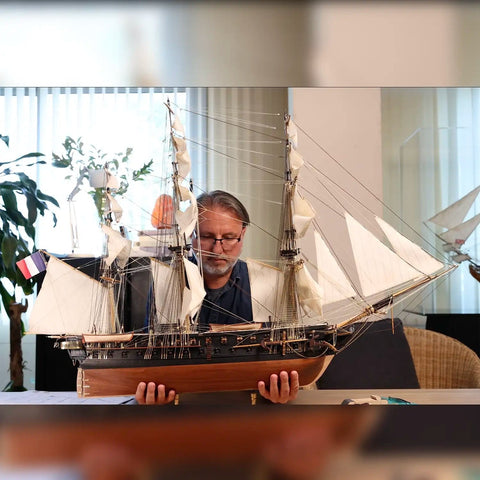 Laivo modelis medinis, tamsaus korpuso ir baltų burinių, didelio mastelio, meistro laikomas rodant tikrą mastelį ir detalumą