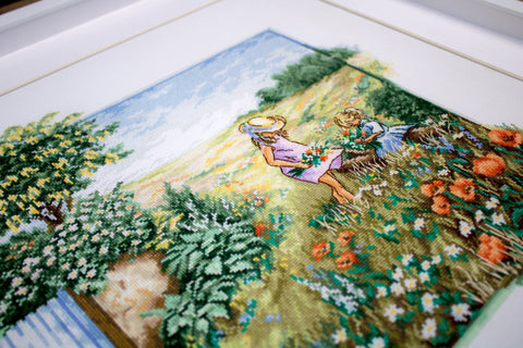 Kryželių siuvinys vaikų pievoje, rėmuotas, kampinis artinimas parodo smulkias siūlių detales ir ryškias spalvas