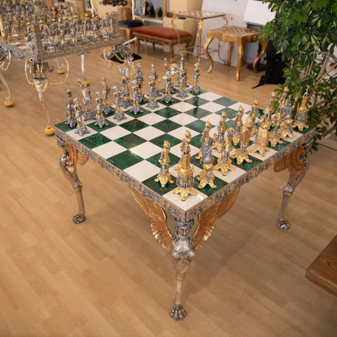Šachmatai ant žalio ir balto malachito lentos su auksuotomis ir sidabruotomis figūrėlėmis, trijų ketvirčių kampu matomos sparnuotos kojų ir ornamentų detalės