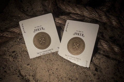 Kortos Joker, U.S. Playing Card Co., baltos su auksiniu heraldiniu ženkleliu, dvi kortos pasvirusios ant smėlio šalia virvės