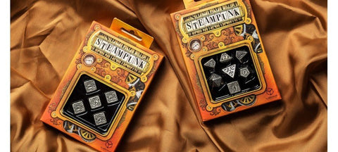 Steampunk kauliukai — du rinkiniai ant auksinio audinio: kairėje metaliniai kvadratiniai kauliukai, dešinėje 7 dalių polihedralų rinkinys
