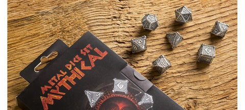 Metaliniai kauliukai Mythical sidabriniai 7 dalių rinkinys su runomis, išmėtyti šalia dėžutės ant medinės lentos