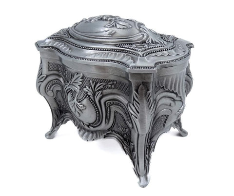 Papuošalų dėžutė sidabro spalvos, baroko raižiniais, trijų kojelių bazė ir išlenktas dangtis, matoma iš priekio-šono