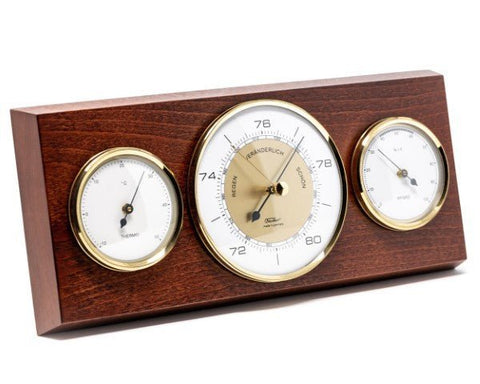 Barometras trijų prietaisų komplekte ant rudos medinės plokštės su auksinio atspalvio žiedais, matuoja slėgį, temperatūrą ir drėgmę