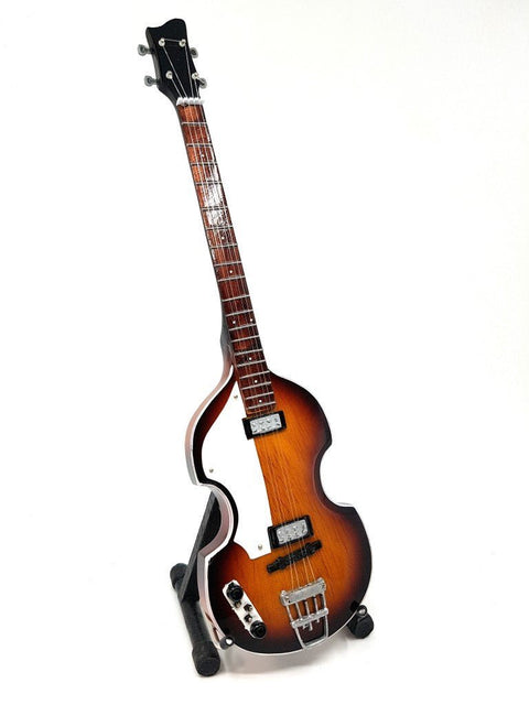 elektrinė gitara saulės atspalvio violoninės formos korpusu, dviem pikapais ir rudu riešuto kakleliu, stovelyje, pateikta kampiniu priekiniu planu