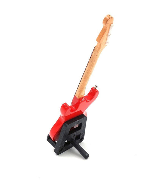 Mini elektrinė gitara raudona, ant mažo juodo stovo, šoniniu kampu rodoma iš užpakalio su matomu kaklu