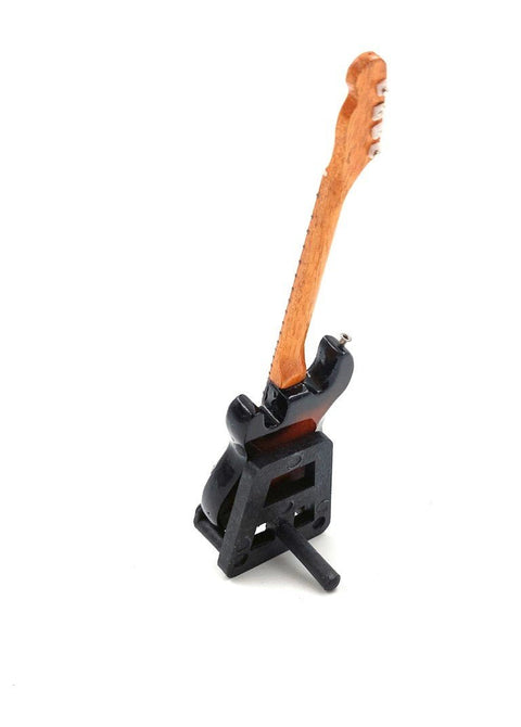 Miniatiūrinė gitara juodu korpusu ir mediniu kaklu ant mažo stovo, rodoma kampu kaip unikalus galerijos variantas