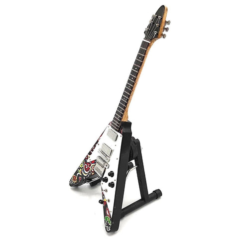 Elektrinė gitara Flying V su balta pickguard, mediniu kaklu ir spalvotu paisley raštu ant sparno, eksponuota ant juodo stovo