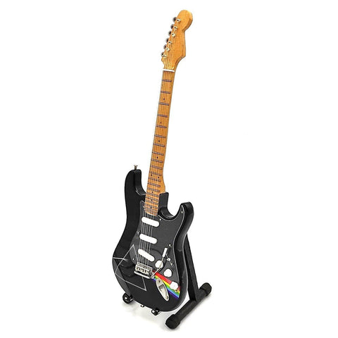 Elektrinė gitara juoda su šviesiu liepos kaklu, trim baltais pikapais ir vaivorykštės lipduku, stovinti ant stovelio kampu