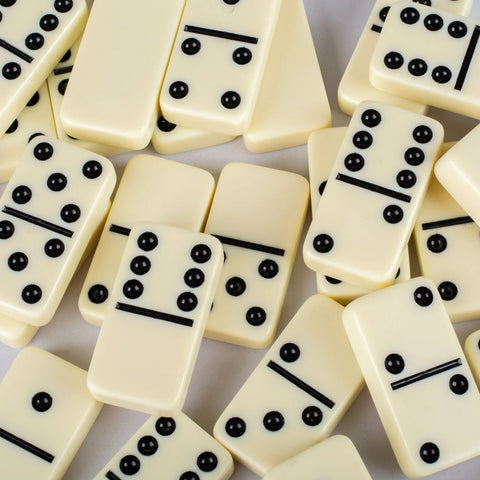 Domino kauliukai kreminės spalvos su iškiliais juodais taškais, arti sudėliota kompozicija pabrėžia paviršiaus faktūrą ir taškų profilį