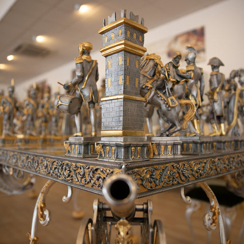 Šachmatų rinkinys ant dekoratyvaus vežimo, sidabro ir aukso tonų detalizuotas bokštas iš arti su patrankos vamzdžiu ir ornamentu