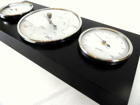 Meteorologinė lenta su trimis chromuotais prietaisais — barometru, termometru ir higrometru, arti fotografuota kampu