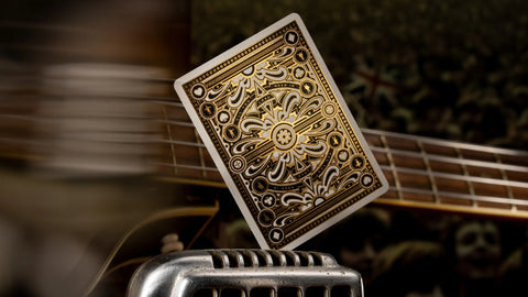 Kortos ornamentuota auksinė–juoda nugarėlė, rodoma iš arti pasvirusiu kampu virš mikrofono ir gitaros stygų