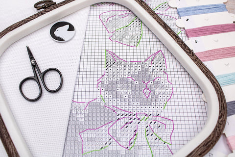 Kryželių raštas su kačiuko piešiniu spausdintu tinkleliu, matomas arti lankelio su spalvų žymėjimais ir siuvimo žirklėmis