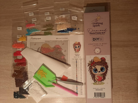 Deimantinė tapyba Crafting Spark „Ežys“ 15×20 cm rinkinys, iš viršaus matomi suskirstyti spalvoti akmenukai, pincetas, žali piltuvėlis ir lipnus plotelis