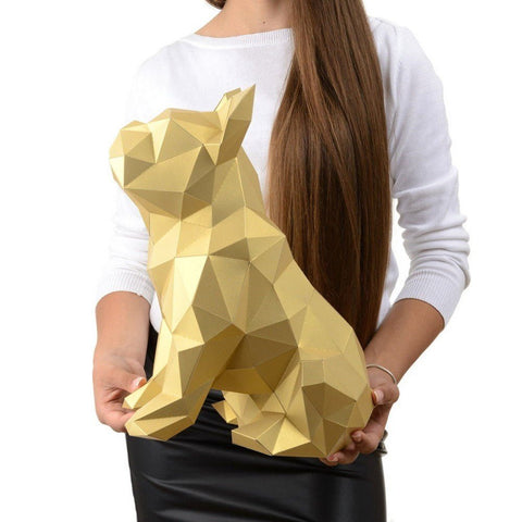 Popierinė katės skulptūra auksinė geometrinė 3D figura, sėdinčio katino siluetas, modelis laiko rankose rodydamas dydį