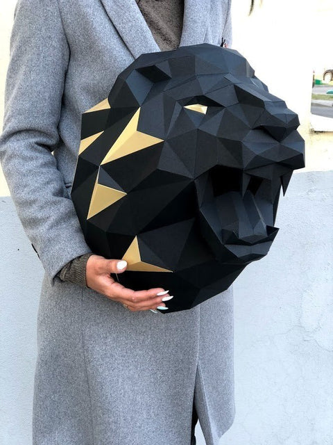 Sieninė liūto galva juoda su auksinėmis geometrinėmis detalėmis, laikoma rankose parodyti mastelį