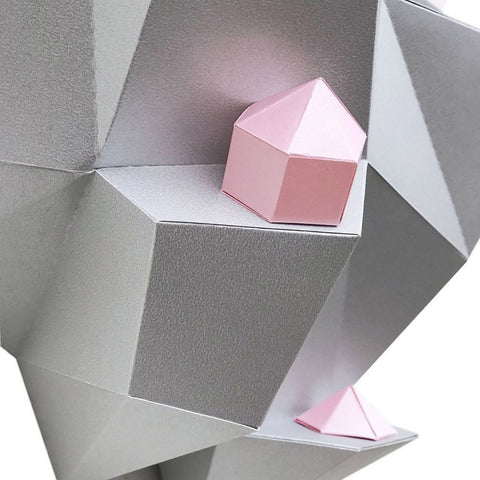 Geometrinė sieninė lentyna sidabrinės faktūros, rodoma iš arti su mažomis rožinėmis geometrinėmis dėžutėmis ir piramide ant skirtingų pakopų