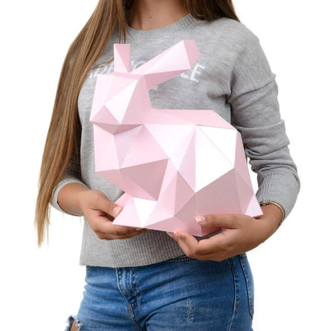 Popierinis triušis rodomas rankose, rausvas geometrinis 3D dekoracijos variantas, parodo tikrą dydį ir formą
