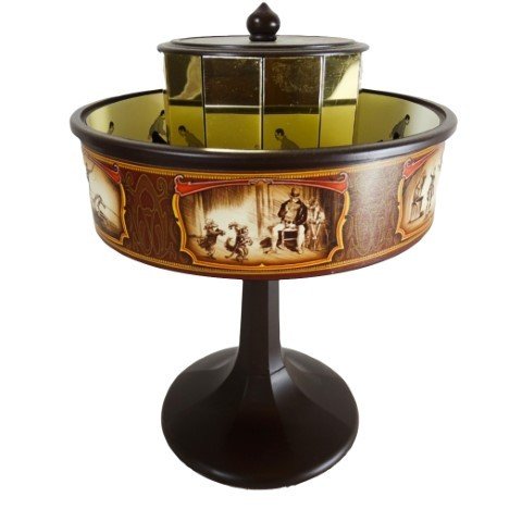 Stalo karuselė rudos ir aukso spalvos su sepia iliustracijų juosta, ant juodo postamento, matoma veidrodinė vidinė mechanika