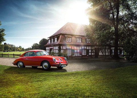Porsche 356 raudonas kupė, klasikinis modelis fotografuotas 3/4 profilyje prie tradicinio namo, skirtas kolekcininkams ir interjero scenarijams