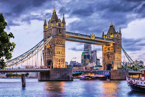 Londono ekskursija: apšviestas Tower Bridge vakaro šviesose su Temzės atspindžiais ir praplaukiančiu kruiziniu laivu