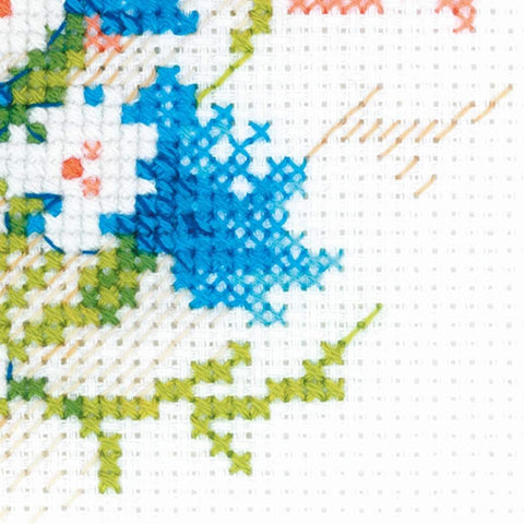 Kryželių siuvinėjimas – artimas mėlynos gėlės ir žalios lapijos siūlių detalės ant baltos drobės.