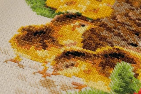 Siuvinėjimo rinkinys, artimas kadras geltonų ir rudų siūlų kryželių ant drobės su matomomis nepabaigtomis vietomis