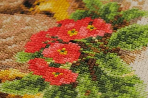 Kryželių rinkinys – artima raudonų gėlių ir žalių lapų siūlų tekstūros detalė ant 14ct drobės, rankų darbo variantas