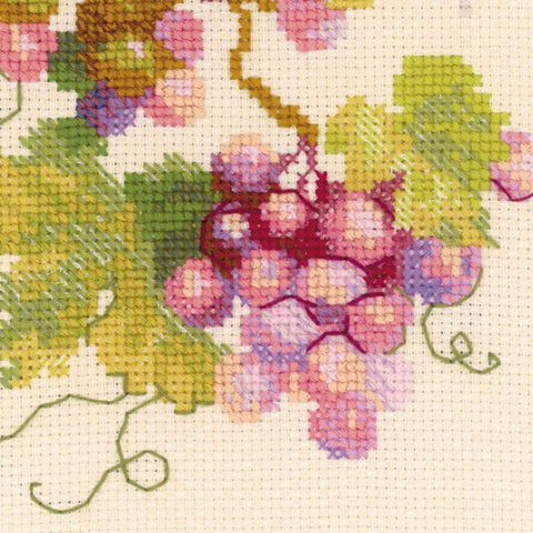 Kryželių siuvinėjimo rinkinys — artima pastelinių rožinių ir žalių vynuogių bei lapų detalė ant smėlio spalvos audinio