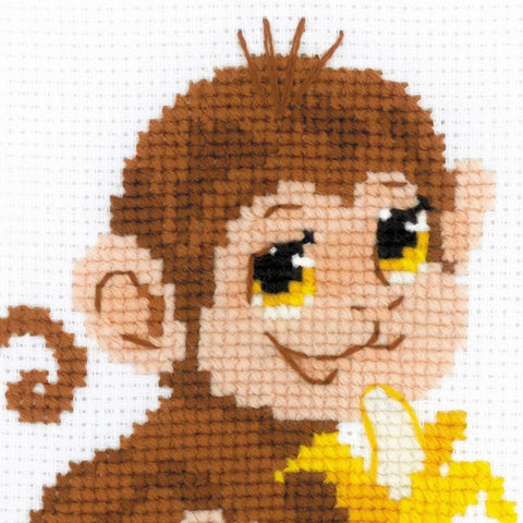 kryželių rinkinys su beždžione, arti siuvinėta ruda galva ir geltona banana ant balto aida audinio, detalus artinys