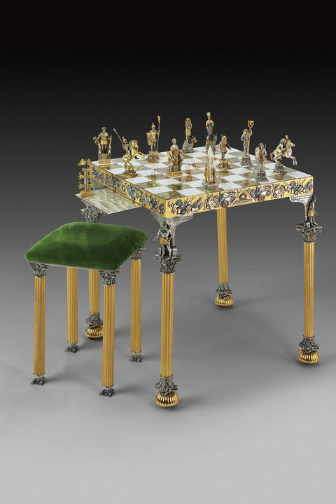 Šachmatų stalas su aukso ir sidabro figūromis ant inkrustuotos marmurinės lentos ir žaliu aksominiu taburetu, matomas iš kampo
