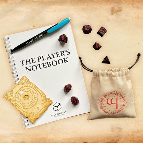 Poliedriniai kauliukai raudonai–juodi su smėlio spalvos drobiniu maišeliu ir spiraliniu „The Player’s Notebook“ užrašų bloku, viršutinis kampo vaizdas