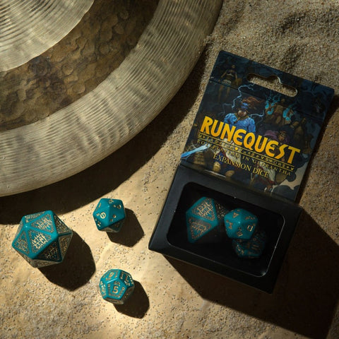 RuneQuest kauliukai – žalsvai turkio ekspansijos rinkinys su auksiniais skaičiais, keli kauliukai išdėstyti prie atverstos pakuotės