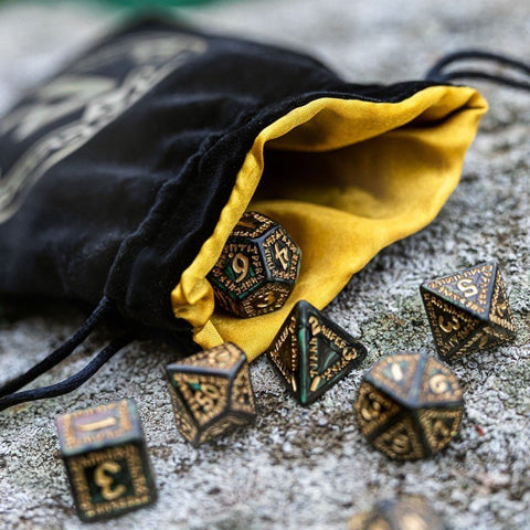 RPG kauliukai 7 v. bronziniai su žalia patina, išdėstyti prie juodo aksominio maišelio su geltonu pamušalu