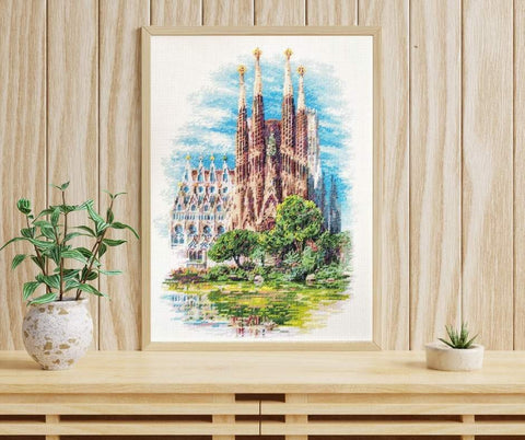 Paveikslas ant drobės su šviesiu mediniu rėmu (A3), Sagrada Familia piešinys mėlynais ir žaliais tonais, eksponuotas ant konsolės šalia kambarinių augalų