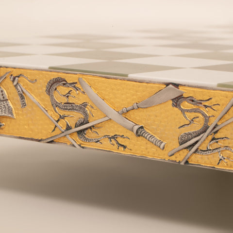 Šachmatų lenta su auksuotu šono apvadais, reljefiniais drakonais ir sukryžiuotais kardais, artimas kampo užfiksavimas