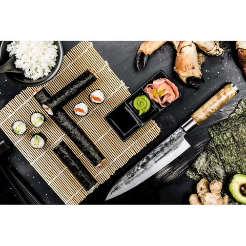 Sushi peilis kalvio rašto plieno geležte ir šviesia medine rankena, pateiktas šalia maki ritinėlių ant bambukinio kilimėlio
