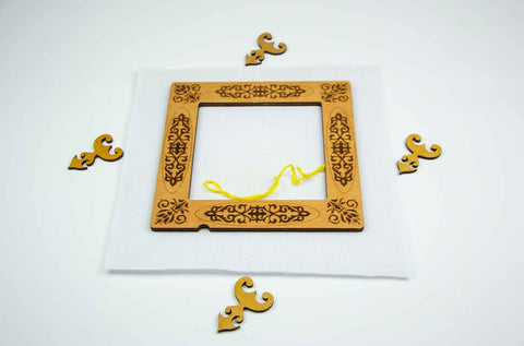 Siuvinėjimo rėmelis medinis kvadratinis su išgraviruotais ornamentais, centre drobė su geltona siūle