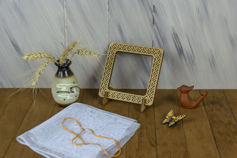 Medinis rėmas su ornamentine išpjauta kraštine, natūralios ąžuolo spalvos, stovintis ant stalo kampu, matomas stovas ir detalės