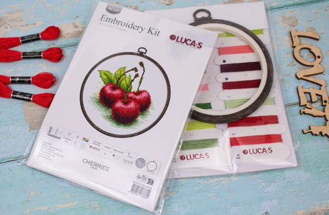 Siuvinėjimo rinkinys LUCA‑S "Cherries" su mediniu lankeliu ir keliomis spalvotomis siūlų kortelėmis, supakuotas, fotografuotas iš viršaus ant melsvo fono